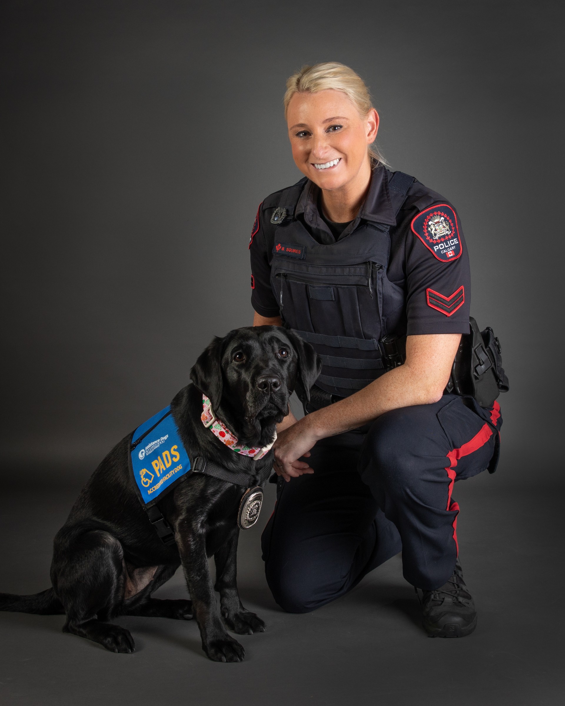AFD Tetris, a shiny black Lab in a blue PADS vest, sits next to her handler, Beckie, a CPS officer.